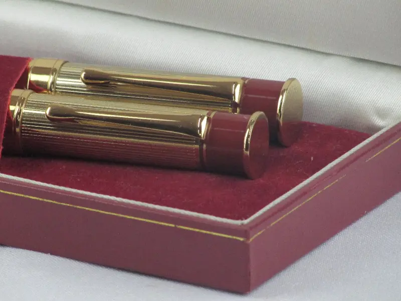 Foto de um(a) Par de canetas LUCKY, da categoria de Outros objetos decorativos. Par de canetas no estojo original da marca LUCKY. Em fino acabamento dourado com detalhes em bordô, uma dela sendo tinteiro.... Mostrado de uma perspectiva diferente. Vendido no marketplace Trésors.