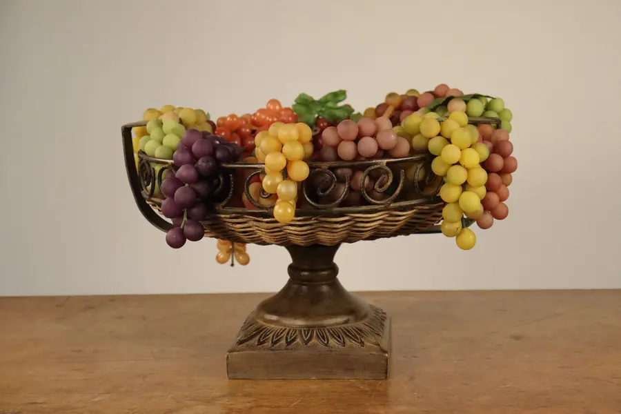 Foto de um(a) Centro de mesa em vime com pedestal e uvas decorativas, da categoria de Centro de mesa. Dimensões de 29,0 cm de altura, 44,5 cm de largura e 43,0 cm de comprimento. Composto por uma cesta trançada em vime... Mostrado de uma perspectiva diferente. Vendido no marketplace Trésors.
